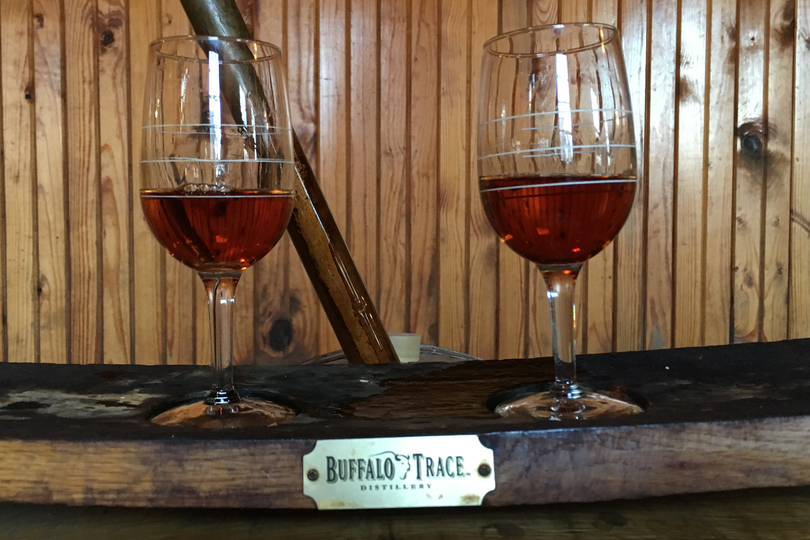 Two stemmed glasses of Eagle Rare 10 Year bourbon resting on a barrel stave